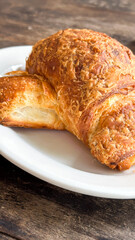 Golden brown croissant on white plate with crispy layers on wooden table, concept of bakery, cafe, breakfast business