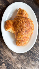 Flaky croissant on rustic wooden table: concept of bakery, breakfast menu, cafe promotion
