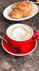Delicious latte in red cup with croissant on rustic table - coffee shop, bakery, café concept