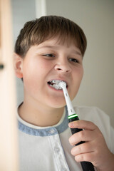 Smiling boy brushing teeth with an electric toothbrush and braces. Concept of oral hygiene, dental care, and orthodontic cleaning for kids.

