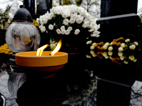 płonący znicz stojący na granitowym grobie