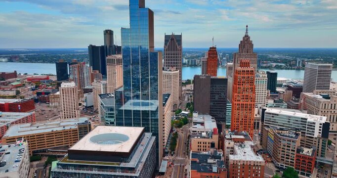 Flying closer to the glass skyscraper in the downtown of Detroit, Michigan, USA. Waterscape of the Detroit River at backdrop.