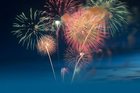 Vibrant colorful fireworks exploding in the dark night sky with a subtle blue cloud effect 