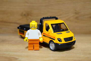 Obraz premium Lego figure stands next to a yellow toy tow truck on a wooden surface
