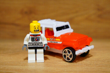 Obraz premium Lego astronaut figure standing next to a toy fire truck on a wooden surface