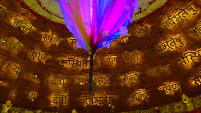 Radiant Hindu prayer dome with glowing multicolor floral chandelier and golden Sanskrit shloka inscriptions curving around the temple ceiling