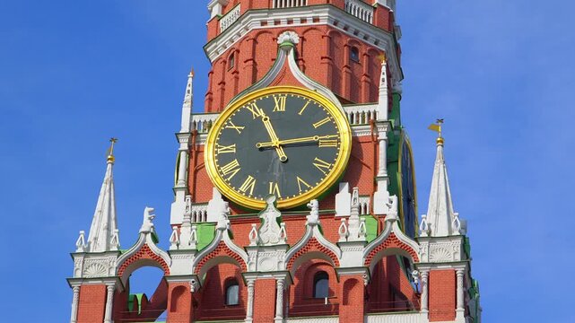 Spasskaya Tower clock on Moscow Kremlin with golden face and Roman numerals against red brick architecture. Famous Russian landmark timepiece showing historic ornate design under clear blue sky.