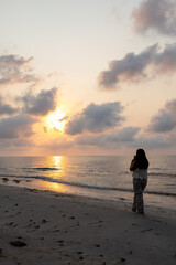 Woman on the beach taking pictures of the sunrise.