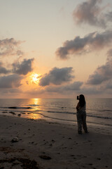 Woman on the beach taking pictures of the sunrise.