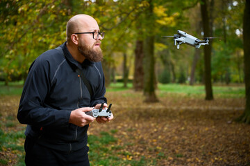 In a serene forest filled with golden autumn leaves, a man skillfully controls his drone, enjoying the tranquility of nature while flying his gadget high above.