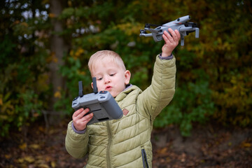 Excited and focused, a young boy operates a drone while holding a controller. Vibrant autumn leaves create a colorful backdrop in the park.
