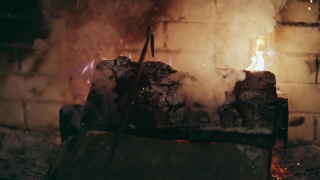 Person setting the glowing fireplace with embers and flying spark flames lighting the brick interior
