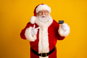 Santa holds a credit card and points with a friendly smile on a bright yellow background celebrating Christmas shopping and holiday magic