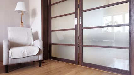 Cozy modern living room interior with beige armchair, wooden floor, and frosted sliding doors. Minimalist home design with warm natural light and calm atmosphere