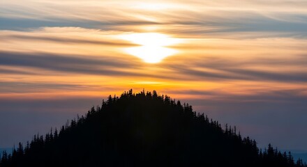 Obraz premium Dramatic sunset silhouette of a pine tree covered mountain peak with vibrant orange and yellow sky
