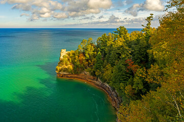 Elevated view of Miners Castle surrounded by turquoise waters of Lake Superior with billowing clouds on horizon.