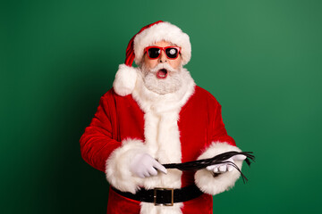 Santa in red costume with hat beard and sunglasses holds a black feather prop in a festive green studio background for a merry holiday stock image
