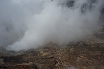 Ethereal landscape with geothermal activity creates a moody and dramatic scene, thick fog and steam veiling a desolate, brown terrain of otherworldly beauty and mystery.