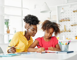Mother and daughter doing homework at home. Mom and teenage black girl happy writing. Teen girl and parent sitting at home working at the table