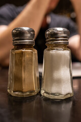 Glass salt and pepper shakers on dark restaurant table under warm evening lighting. Simple detail of everyday dining atmosphere.