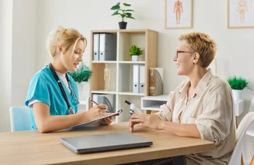 Fotobehang Leder Happy senior patient and nurse on geriatric care appointment in clinic. Young doctor listening to smiling old woman talking about symptoms, general practitioner writing notes on consultation  © Studio Romantic