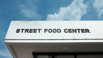 Street Food Center word sign displayed on a commercial or public market building under a clear blue sky, symbolizing culinary variety, casual dining, local cuisine, vendors, and vibrant urban eating