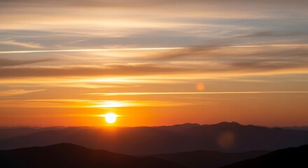 Fototapeta premium Vibrant orange and yellow sunset paints the sky over silhouetted mountain peaks at dusk