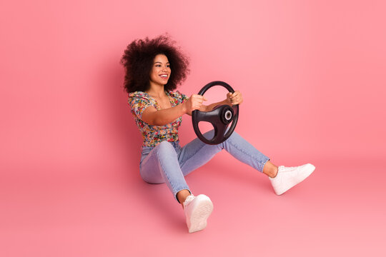 Fototapeta Cheerful young woman holding a steering wheel against a pink background exuding positivity, fun and vibrant energy