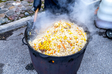 Cooking appetizing traditional pilaf with meat in a large cauldron outdoors