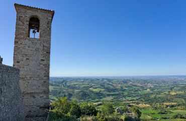 View over the rolling hills of Emilia Romagna with a small medieval tower/ruin perched on a rocky cliff.