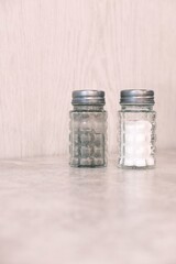 Pair of glass salt and pepper shakers with waffle or grid pattern and metal tops. Dispensing salt and pepper in restaurants, cafes or at home. Kitchen accessories. Vertical image with copy space