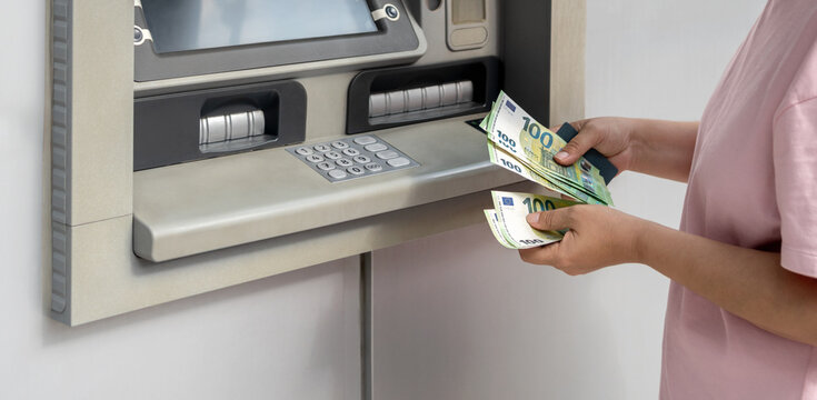 Woman withdrawing euro banknotes from an ATM, holding cash and bank card. Concept of euro currency, cash withdrawal, modern banking and financial transition in Europe. Horizontal banner