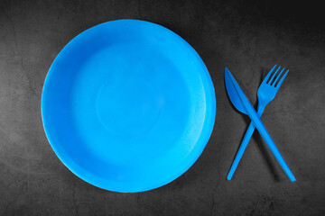 Empty blue plate and cutlery on black background, top view