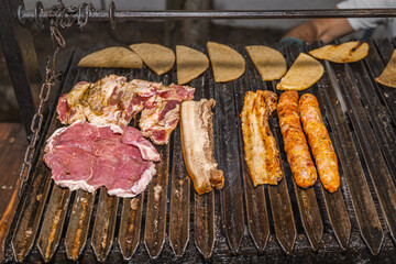 Raw beef, pork belly and chorizos on barbecue with folded arepas in Colombian outdoor cooking scene