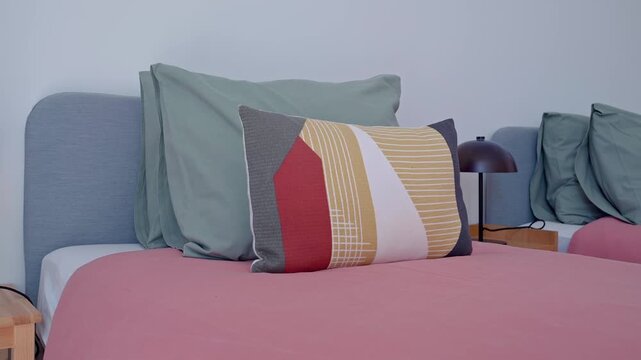 Modern bedroom interior design showcasing two single beds with pink bedspreads, green pillows, and decorative patterned cushions, illuminated by stylish lamps on wooden bedside tables