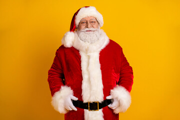 Santa Claus in red suit with white fur hat and belt smiles against a bright yellow background for holiday promotion and festive family mood