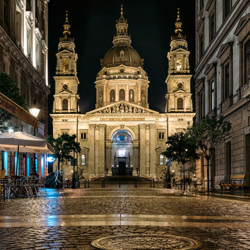 St. Stephen&rsquo;s Basilica at night illuminated by streetlights and reflections on wet cobblestone street in the historic center of Budapest, Hungary