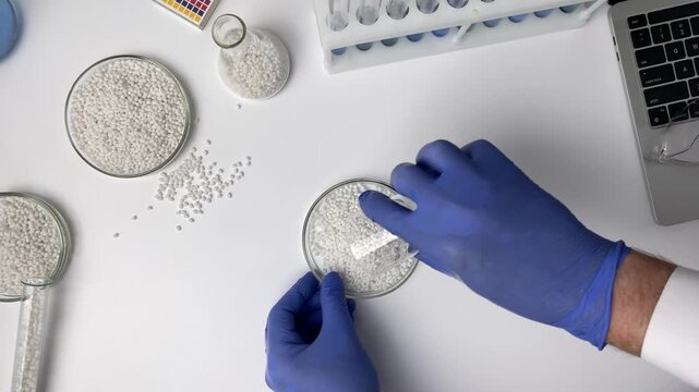 Top view a scientist in a laboratory checks the quality of a samples of white thermoplastic granules. Plastic raw granules materials for industry.