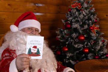 Santa holding Christmas card with tree backdrop