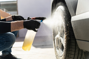Person detailing car wheel with spray bottle