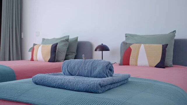 Luxurious hotel bedroom featuring twin beds adorned with teal and pink bedspreads, complemented by neatly rolled blue towels showcasing impeccable guest service and comfortable accommodations