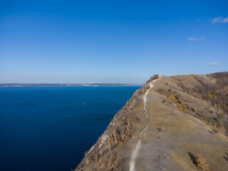 Mountain Ridge Landscape: Aerial view showcases a rugged mountain ridge extending towards the tranquil waters, embraced by a vast expanse of a clear, serene sky, evoking a sense of tranquility.