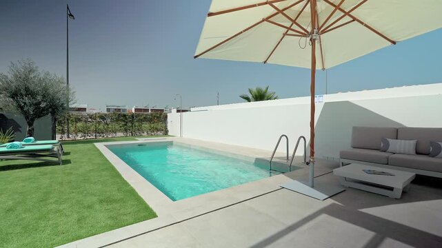 Luxury villa poolside featuring elegant garden furniture, spacious sunbeds, and shading parasol creating peaceful outdoor relaxation setting under bright blue sky