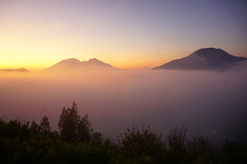 Sunrise over the mountain with fog. New day. Morning view in a foggy mountains. Natural nature landscape backgrounds. Mist mount Batur scenery at dusk. Pinggan Village, Kintamani - Bali, Indonesia