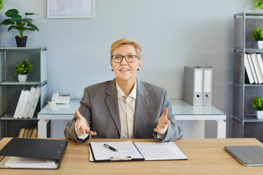 Business coach explaining during online meeting. Smiling woman gestures in office on video call during webinar or conference. Guidance, coaching, technology and clear communication concept.