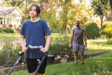 Father watches as son pushes lawnmower