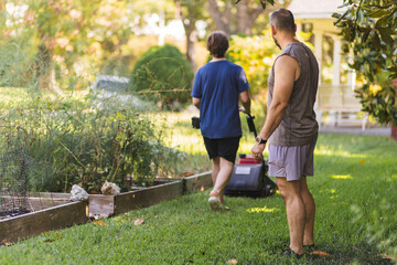 Son is pushing lawnmower while dad is watching