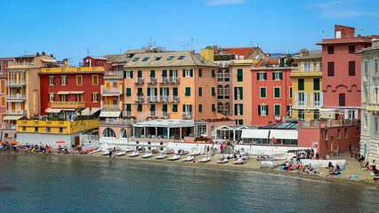 Coastal Charm: Colorful buildings line the shoreline, facing the calm sea under the clear, sunny sky, reflecting the beautiful architecture of the area.