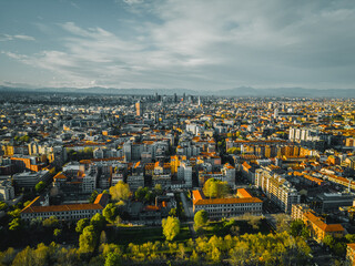 Urban Aerial Panorama: An expansive cityscape unfolds under a vast, cloud-strewn sky, revealing an intricate tapestry of buildings, infrastructure, and urban design.