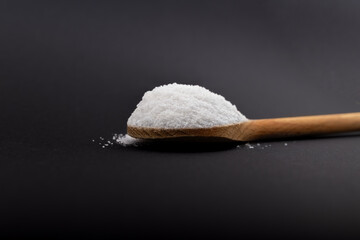 Iodated salt scoop in front of black background with wooden spoon. Textured horizontal photo, closeup. V38.